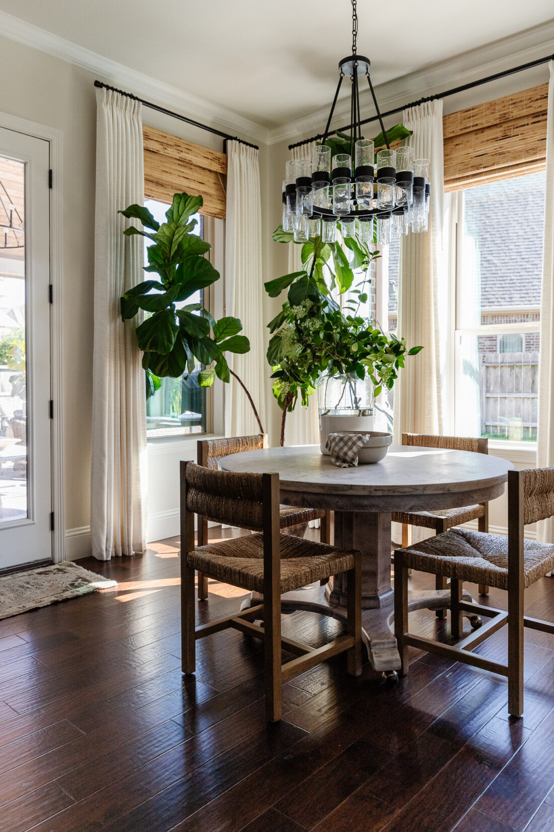 small dining room breakfast nook with round table and pottery barn Malibu woven chairs.  Windows with light drapes and a fiddle leaf fig tree